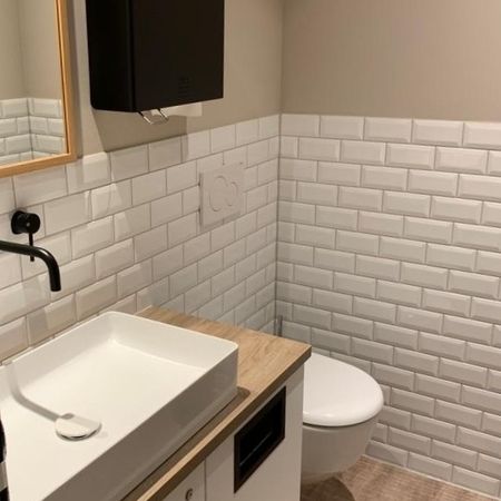 Badezimmer mit weißen Fliesenwänden und einem Waschbecken, das eine saubere und moderne Atmosphäre vermittelt.