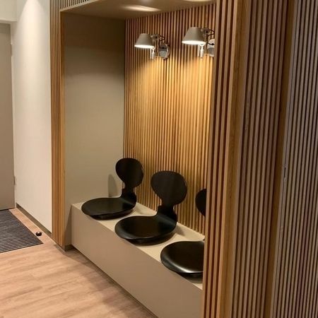 Warteraum mit schwarzen Stühlen und einer Wand aus Holz.
