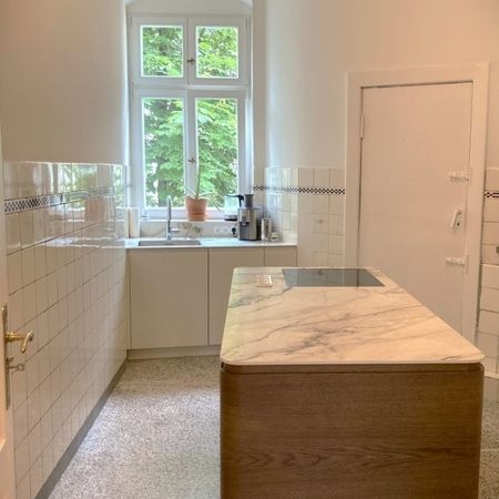 Eine moderne Küche mit einer Marmorinsel und einem großen Fenster, das viel Tageslicht hereinlässt.